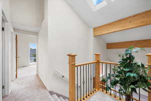 Corridor featuring beamed ceiling, a skylight, light colored carpet, and a textured ceiling