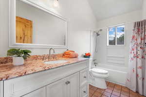 Full bathroom featuring tile patterned flooring, shower / bathtub combination with curtain, vaulted ceiling, toilet, and vanity