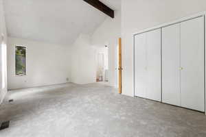 Unfurnished bedroom with ensuite bathroom, light colored carpet, high vaulted ceiling, beam ceiling, and a textured ceiling