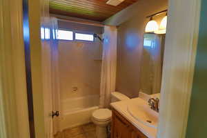 Full bathroom with vanity, wood ceiling, shower / bathtub combination with curtain, tile patterned floors, and toilet