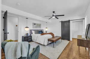 Bedroom featuring light hardwood / wood-style flooring, ceiling fan, and a barn door