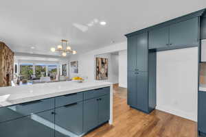 Kitchen featuring an inviting chandelier, hardwood / wood-style floors, light stone countertops, pendant lighting, and blue cabinets