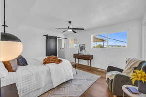 Bedroom featuring dark hardwood / wood-style flooring, ceiling fan, and a barn door