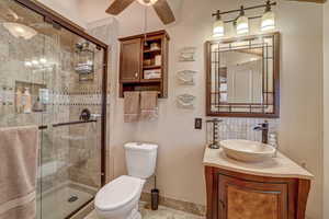 Bathroom featuring vanity, toilet, ceiling fan, and a shower with door