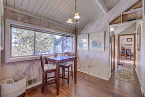 Dining room featuring wood walls, an inviting chandelier, wooden ceiling, hardwood / wood-style floors, and vaulted ceiling with beams