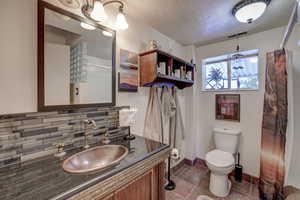 Bathroom with tile patterned flooring, backsplash, toilet, vanity, and a textured ceiling