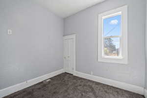 Unfurnished room featuring lofted ceiling and dark carpet