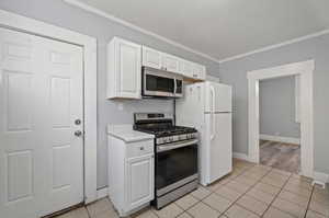 Kitchen with ornamental molding, white cabinets, a textured ceiling, appliances with stainless steel finishes, and light tile patterned flooring