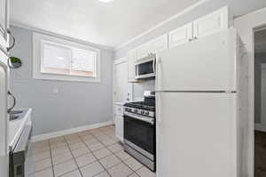 Kitchen featuring a textured ceiling, light tile patterned floors, appliances with stainless steel finishes, crown molding, and white cabinetry