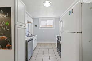 Kitchen with white cabinetry, a textured ceiling, light tile patterned floors, sink, and appliances with stainless steel finishes