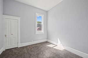 Carpeted spare room featuring vaulted ceiling