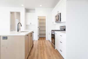 Kitchen featuring an island with sink, tasteful backsplash, white cabinetry, stainless steel appliances, and light wood-type flooring