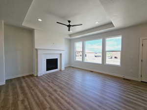 Unfurnished living room with a fireplace, a tray ceiling, dark hardwood / wood-style floors, ceiling fan, and a textured ceiling