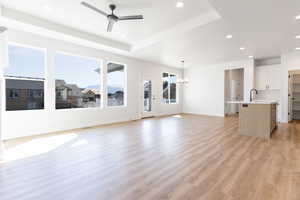 Unfurnished living room featuring ceiling fan with notable chandelier, light wood-type flooring, a tray ceiling, and sink