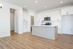 Kitchen featuring light hardwood / wood-style floors, white cabinetry, tasteful backsplash, stainless steel appliances, and a kitchen island with sink