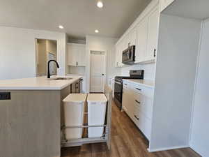 Kitchen with dark hardwood / wood-style flooring, a kitchen island with sink, stainless steel appliances, sink, and white cabinetry