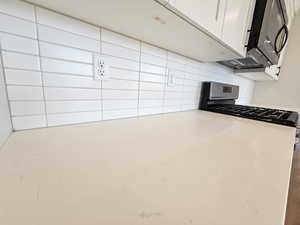 Kitchen featuring backsplash, stainless steel range with gas stovetop, and white cabinetry