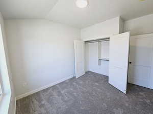 Unfurnished bedroom with lofted ceiling, dark colored carpet, and a closet