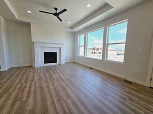 Unfurnished living room featuring a tray ceiling, ceiling fan, a tile fireplace, and wood-type flooring