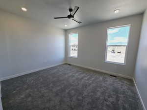 Empty room with dark carpet, ceiling fan, and a textured ceiling