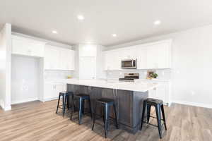 Kitchen featuring a center island with sink, appliances with stainless steel finishes, light hardwood / wood-style flooring, and white cabinetry