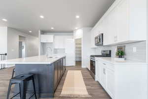 Kitchen featuring appliances with stainless steel finishes, white cabinets, sink, and an island with sink