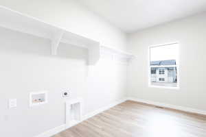 Clothes washing area with light hardwood / wood-style flooring, hookup for a washing machine, and electric dryer hookup