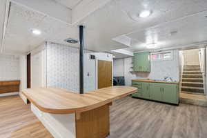 Kitchen with light wood-type flooring, washing machine and dryer, green cabinetry, and sink