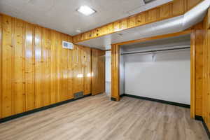 Basement with wooden walls and light hardwood / wood-style flooring