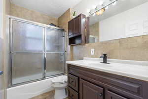 Full bathroom with a textured ceiling, vanity, combined bath / shower with glass door, toilet, and decorative backsplash