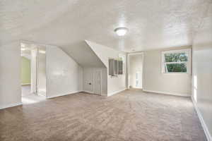 Additional living space featuring vaulted ceiling, a textured ceiling, heating unit, and light colored carpet