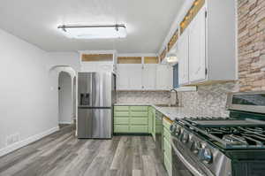 Kitchen with white cabinets, light wood-type flooring, appliances with stainless steel finishes, sink, and a textured ceiling