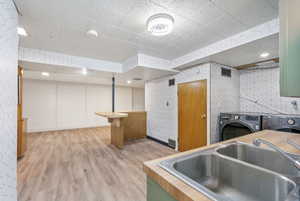 Kitchen featuring green cabinetry, wood counters, hardwood / wood-style floors, washer and dryer, and sink