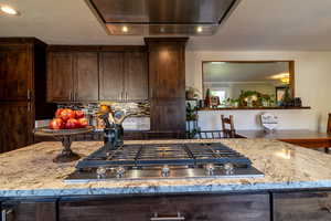 Kitchen with stainless steel gas stovetop, light stone counters, exhaust hood, and decorative backsplash