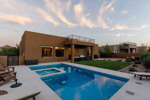 Pool at dusk featuring a patio area, a lawn, and an in ground hot tub