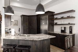 Kitchen with decorative light fixtures, light stone counters, kitchen peninsula, decorative backsplash, and light hardwood / wood-style floors