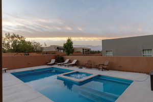 Pool at dusk featuring an in ground hot tub and a patio