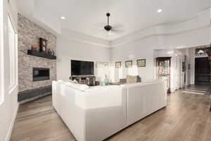 Living room featuring a raised ceiling, light hardwood / wood-style floors, ceiling fan with notable chandelier, and a fireplace