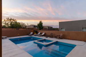 Pool at dusk featuring an in ground hot tub and a patio