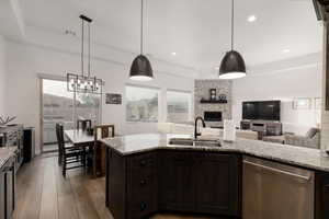 Kitchen featuring dishwasher, a fireplace, light stone counters, sink, and pendant lighting