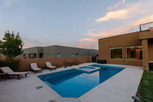 Pool at dusk with a patio area and an in ground hot tub