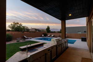 Patio terrace at dusk with a grill, a fenced in pool, and an outdoor kitchen