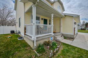 Doorway to property featuring a yard, a porch, and central AC unit