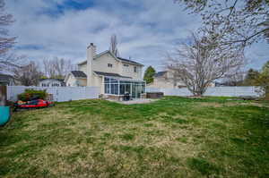 Rear view of house featuring a sunroom, a lawn, and a patio area