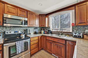 Kitchen featuring light wood-type flooring, tasteful backsplash, stainless steel appliances, and sink