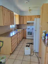 Kitchen featuring sink, light tile patterned floors, white appliances, and light brown cabinets