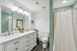 Bathroom with wooden walls, hardwood / wood-style floors, walk in shower, toilet, and vanity