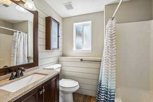 Full bathroom featuring wooden walls, hardwood / wood-style floors, toilet, shower / tub combo with curtain, and vanity