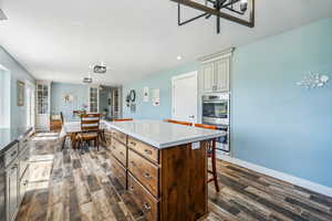 Kitchen with cream cabinetry, a kitchen bar, a center island, double oven, and dark wood-type flooring