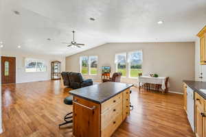 Kitchen with a kitchen island, vaulted ceiling, light hardwood / wood-style flooring, and dishwasher